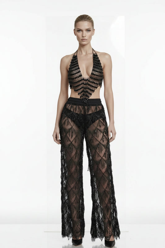 A model wearing a black sheer lace halter crop top and matching wide-leg pants with a geometric diamond lace pattern, set against a plain white background.