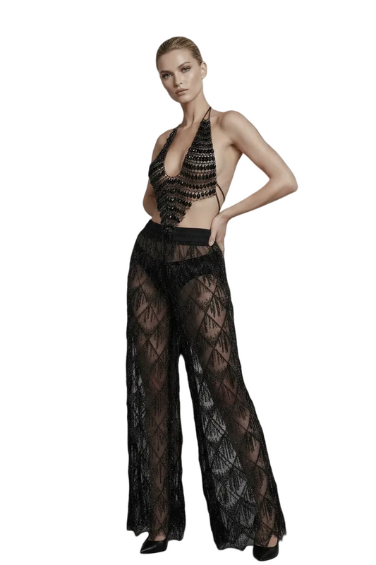 A model wearing a black sheer lace halter top and matching wide-leg sheer lace pants, posed against a solid black background.
