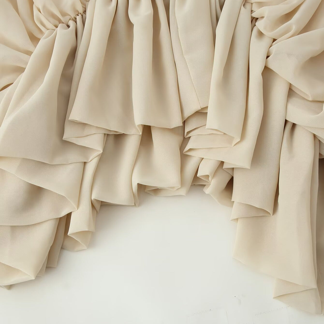 Beige draped fabric with a ruffled, tiered edge, shown against a plain white background.